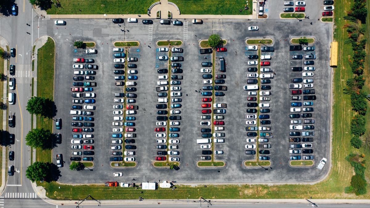 Luftaufnahme eines Parkplatzes mit hellen Fahrzeugen in Reihen nahe Rasenflächen